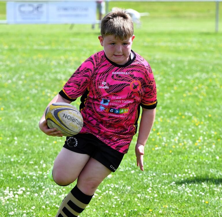 A junior player running with the ball in the pink Aspatria Hornets kit